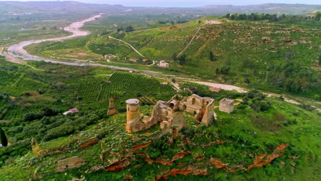 Aerial-forwarding-shot-of-ruins-of-an-old-building-over-hilly-terrain-with-a-winding-river-flowing-in-the-background-in-north-of-Troina,-Sicily,-Italy-at-daytime