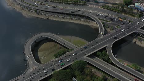 Aerial-panning-shot-above-complex-road-system-connecting-bridges-on-and-off-ramps-and-loops-over-canal-and-river-in-Ho-Chi-Minh-City,-Vietnam-on-a-sunny-day