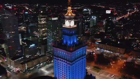 Aerial-view-of-the-illuminated-Palace-of-Culture-and-Science-in-Warsaw,-Poland---reverse,-tilt,-drone-shot