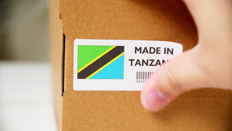 Hands-applying-MADE-IN-TANZANIA-flag-label-on-a-shipping-cardboard-box-with-products