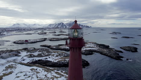 Beautiful-aerial-pedestal-shot-of-the-Andenes-Lighthouse-in-Norway-with-the-snow-speckled-rocky-shore-and-mountains-in-the-background