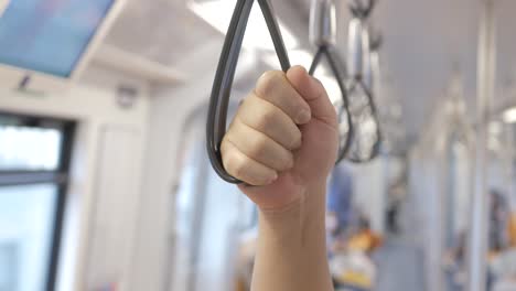 Close-up-of-Hands-holding-handrail-or-grip-straps-in-metro-train,public-subway-transportaion-train