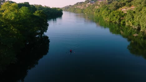 Kayaker-paddling-through-glassy-water-during-sunrise-in-Austin-Texas,-drone-pull-away-to-reveal-downtown-skyline-from-Redbud-Isle-nature-trail