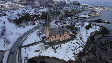Magnificent-aerial-orbit-of-Kabelvag-Church-in-winter-with-snow-covered-mountains-in-the-background,-Lofoten-Cathedral