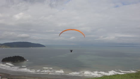 Paraglide-pilot-launches-from-grass-ramp-high-above-cloudy-beach