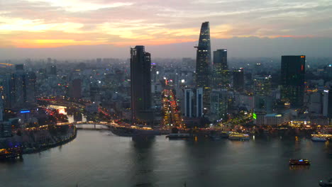 Ho-Chi-Minh-Stadt-Vietnam-Bei-Sonnenuntergang,-Luftaufnahme-Der-Stadtlandschaft-Am-Saigon-Fluss-Am-Abend,-Gebäude,-Wolkenkratzer,-Straßen,-Brücken-Und-Goldener-Himmel-Im-Hintergrund