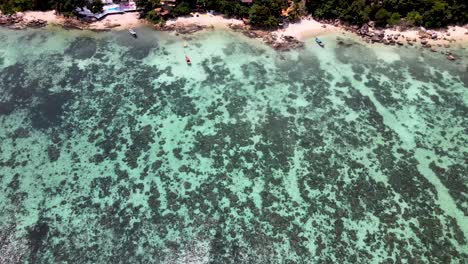 Overhead-Aerial-Over-Tranquil-Coral-Waters-Towards-Beach-At-Koh-Lipe