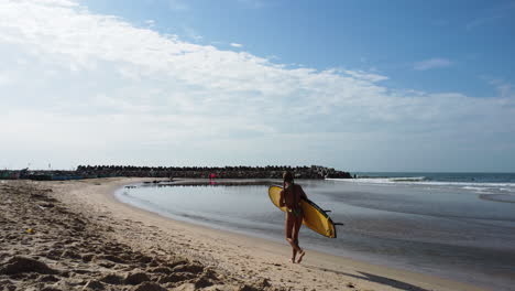 A-young-lady-in-a-swimsuit-is-carrying-a-yellow-surfboard