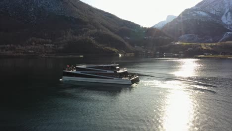 Elektrisches-Passagierboot,-Sicht-Auf-Die-Fjorde,-Die-Rückwärts-Segeln,-Nachdem-Sie-Touristen-Einen-örtlichen-Wasserfall-In-Flam-Gezeigt-Haben-–-Statische-Antenne-Mit-Sonnenlichtreflexionen-In-Der-Meeresoberfläche-Und-Auf-Dem-Boot