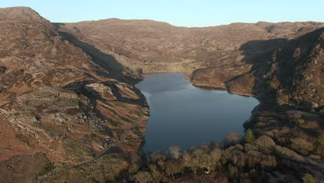 An-aerial-vioew-of-Liyn-Cwm-Bychan-lake-as-the-sun-begins-to-set,-flying-right-to-left-around-the-end-of-the-lake,-Gwynedd,-North-Wales,-UK