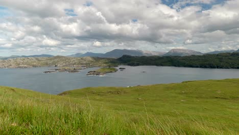 A-wide-landscape-view-of-the-mountains-and-rocky-coastline-of-North-Scotland-with-lush-green-grass-and-slowly-moving-clouds,-filmed-on-Handa-Island