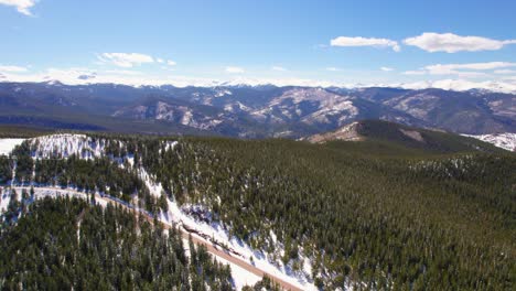 Aerial-Drone-Establishing-Shot-Flying-Over-Snowy-Alpine-Forest-Hills-With-Rocky-Mountains-Range-In-The-Background-Near-Mount-Evans-Colorado-USA