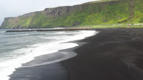 Black-sand-beach-with-waves-in-Vik,-Iceland-with-drone-video-moving-forward