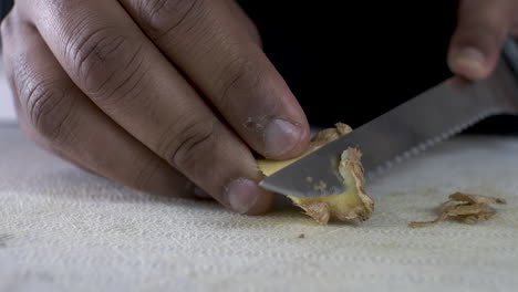 Hand-Of-Ethnic-Minority-Adult-Male-Using-Serrated-Knife-To-Peel-Skin-Off-Ginger-On-Cutting-Board