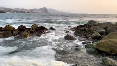 Tilt-up-reveal-shot-of-sea-shore-with-hill-range-view-at-background-in-San-Bartolo,-Lima,-Peru