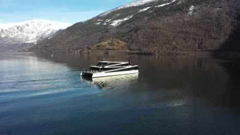 Aerial-rotating-around-electric-hybrid-sightseeing-boat-full-of-tourists-in-Aurlandsfjorden---Vessel-reversing-on-water-with-many-tourists-standing-outside---Flam-Norway