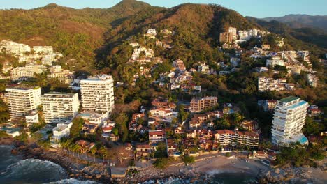 Hotels-on-mountain-coastline-in-Playa-Amapas,-Puerto-Vallarta-Mexico-at-sunset,-aerial