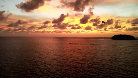 Luftaufnahme-Eines-Parasailers,-Der-Von-Einem-Boot-Gegen-Den-Goldorangefarbenen-Sonnenuntergangshimmel-über-Tropischen-Gewässern-Vor-Phuket-Gezogen-Wird