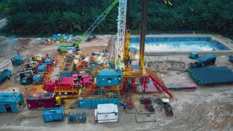 Cinematic-Drone-Shot-of-Onshore-Drilling-and-Workover-Rig-structure-and-Rig-equipment-for-oil-exploration-and-exploitation-in-the-middle-of-jungle-surrounded-by-palm-oil-trees-during-sunset-time