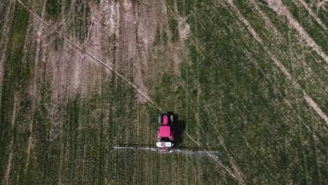 Aerial-view-of-farming-tractor-spraying-on-field-with-sprayer,-herbicides-and-pesticides-insecticide-to-the-green-field-plowed-land,-steady-top-down-shot