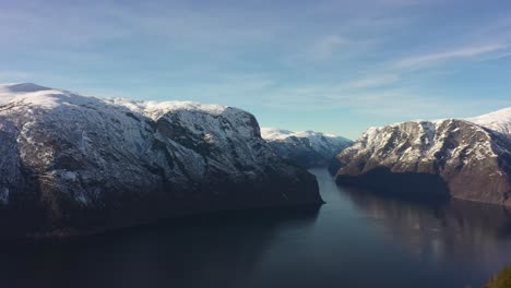 Flying-over-person-walking-towards-tip-of-Stegastein-viewpoint-above-Aurlandsfjord---Forward-moving-aerial-passing-viewpoint-and-flying-into-vast-mountain-landscape-above-fjord---Norway