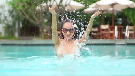Close-up-of-a-young-woman-playfully-splashing-pool-water-into-the-air