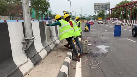 Construction-workers-drill-holes-at-a-road-divider-on-a-busy-road-in-New-Delhi