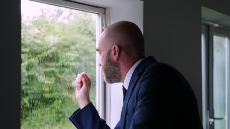 An-anxious-worried-businessman-is-stressed-with-head-in-hands-while-he-is-looking-out-of-a-window-at-the-rain