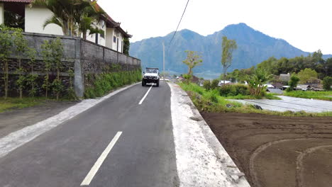 Jeep-4wd-Conduciendo-Por-Un-Camino-Sinuoso-A-Través-De-Edificios-Y-Campos-De-Arroz-En-Bali,-Indonesia