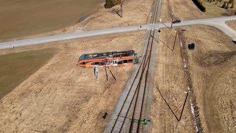 Drone-shot-of-Elron-train-wreck-next-to-railway-between-field,-cars-crossing-railway-on-background