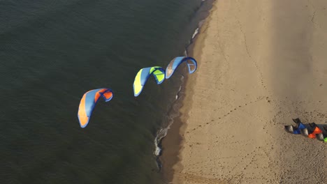 Aerial-drone-oribits-around-3-kiteboarding-kites,-kitesurfing