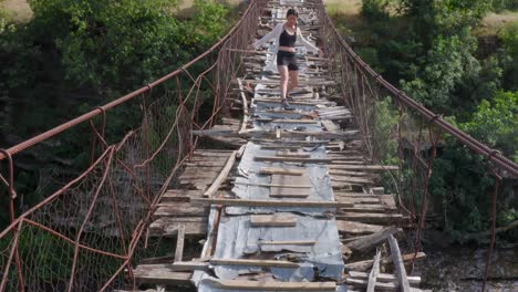 Young-asian-girl-cautiously-crossing-a-wooden-suspension-bridge-in-poor-condition