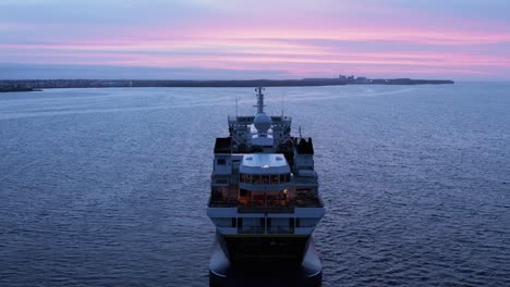 Expedition-cruise-ship-anchored-in-calm-water-near-shore-of-Iceland,-sunset