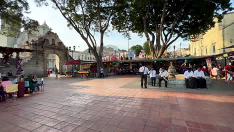 Evento-Tradicional,-Gente-Local-Mexicana-Y-Turistas-Sentados-Reunidos-Junto-A-La-Plaza-De-La-Danza-Oaxaca-Mexico,-Fuente-Exterior-En-La-Explanada-Del-Patio-Rodeada-De-Terrazas-De-Mercado-Y-Café