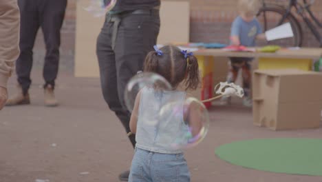 Young-girl-waving-stick-around-while-being-surrounded-with-large-soap-bubbles