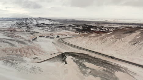 Aerial-Tracking-View-From-Afar-of-Cars-Driving-Moving-on-Curved-Route-Road-in-Winter,-Surrounded-by-Vast-White-Snowy-Northen-Wild-Lands-and-Mountains,-Spectacular-Cinematic-Landscape