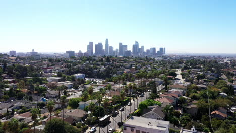 Beautiful-drone-shot-from-a-neighborhood-of-Los-Angeles,-California-showing-palm-trees-and-the-city-skyline