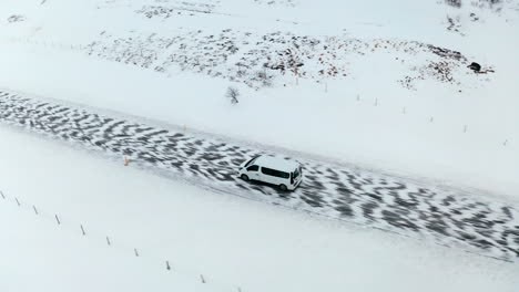 Aerial-tracking-shot-of-Van-on-tour-on-snowy-and-icy-road-on-Iceland-Island-during-bright-day-in-winter