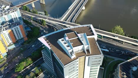 Aerial-view-of-an-office-building-at-the-intersection-of-Coronation-Drive-and-The-Go-Between-Bridge,-drone-slowly-ascends-to-reveal-heavy-traffic-below,-with-the-Brisbane-River-in-the-background