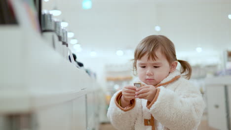 Curious-3-Years-Old-Girl-Picking-A-Gold-Bar-Item-Displayed-Inside-A-Shopping-Mall