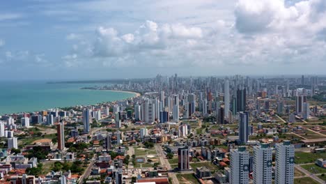 Trucking-left-aerial-wide-shot-of-the-tropical-beach-city-of-Cabedelo,-Brazil-from-the-intermares-beach-near-Joao-Pessoa-with-skyscrapers-along-the-coastline-in-the-state-of-Paraiba-on-a-summer-day