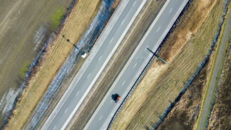 An-overhead-drone-shot-of-a-highway-during-the-winter-with-dead-grass-and-cars-flowing-both-directions-on-the-highway-passing-through-the-frame