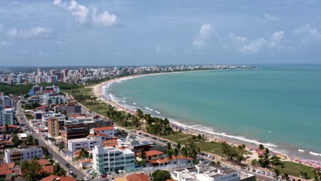 Trucking-left-aerial-shot-of-the-tropical-intermares-beach-in-Cabedelo,-Brazil-near-Joao-Pessoa-with-apartments,-homes,-and-palm-trees-along-the-coastline-in-the-state-of-Paraiba-on-a-warm-summer-day
