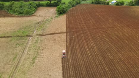 A-reverse-aerial-footage-of-a-tractor-tilling-a-farmland-also-revealing-birds-flying-below-and-a-treeline-in-Muak-Klek,-Thailand