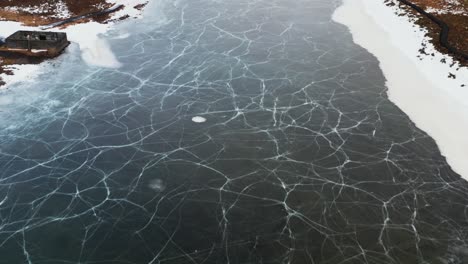 Frozen-Seltjörn-fishing-lake-in-Iceland-during-winter-season-with-cracked-surface,-aerial