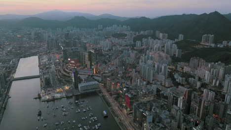 Aerial-panoramic-shot-of-Kowloon-Bay-Area,-Hong-Kong-after-sunset-with-Mountain-range-silhouette-in-background
