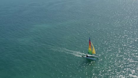 Rising-aerial-shot-following-a-colorful-sail-boat-from-the-tropical-Bessa-beach-in-the-coastal-capital-city-of-Joao-Pessoa,-Paraiba,-Brazil-on-a-warm-sunny-summer-day