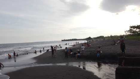 Indonesian-Balinese-People-Bath-at-Local-Beach-of-Black-Sand-and-Cloudy-Sky,-in-Pantai-Purnama,-Sukawati,-Gianyar,-Bali,-Southeast-Asia