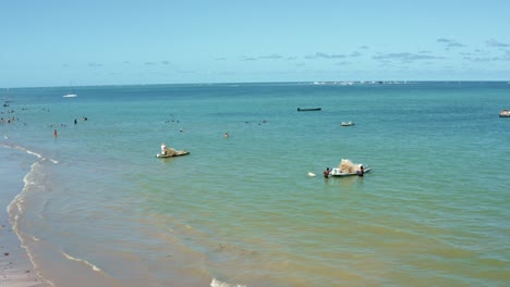 Dolly-in-aerial-shot-of-small-fishing-boats-preparing-to-set-sail-on-the-shore-of-Bessa-beach-in-the-tropical-capital-Joao-Pessoa,-Brazil-in-the-state-of-Paraiba-on-a-warm-sunny-summer-day