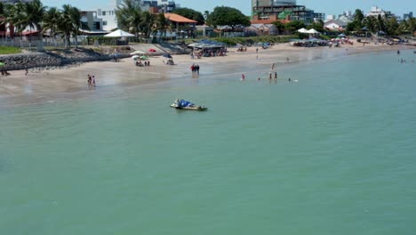 Dolly-in-aerial-drone-shot-of-the-tropical-Bessa-beach-in-the-coastal-capital-city-of-Joao-Pessoa,-Paraiba,-Brazil-with-people-enjoying-the-ocean-and-fishing-boats-at-shore-on-a-warm-sunny-summer-day